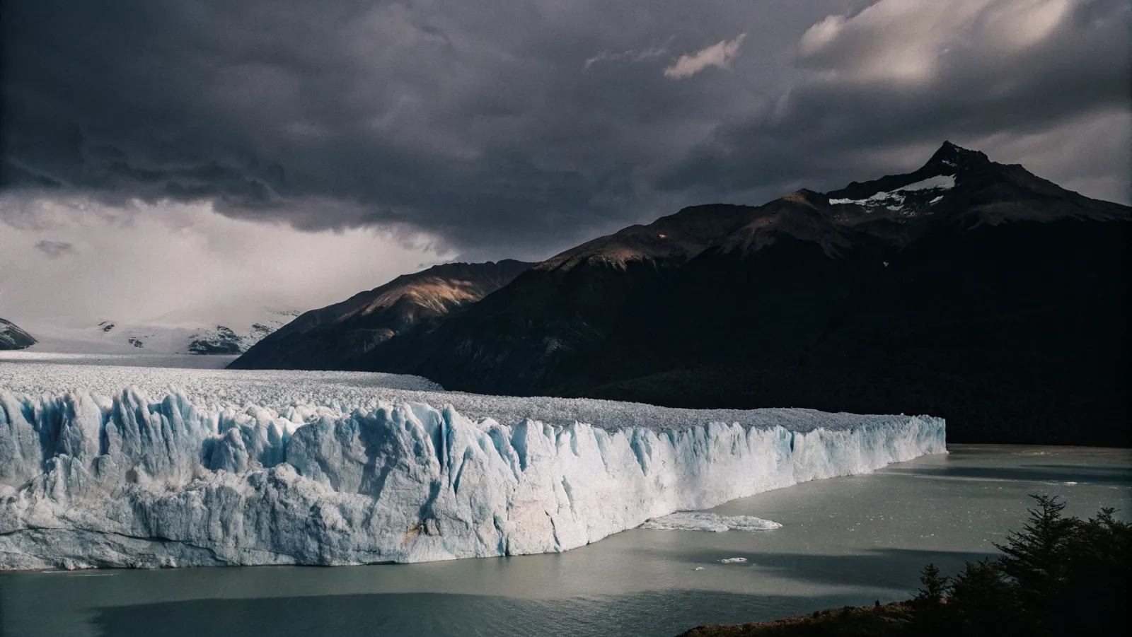 Perito Moreno ledājs Patagonijā ar ziliem ledus blokiem un kalnu fonu