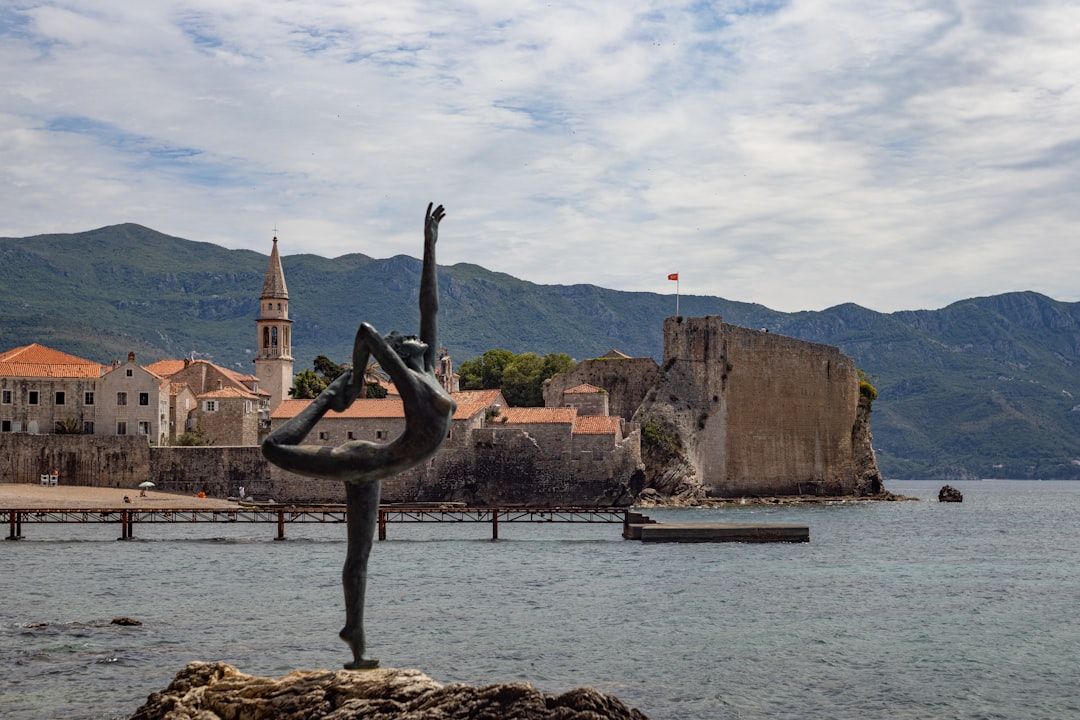 Mogren pludmale — Bronzas balerīnas statuja uz klints ar Budvas vecpilsētu un Citadeli fonā, Melnkalnē.