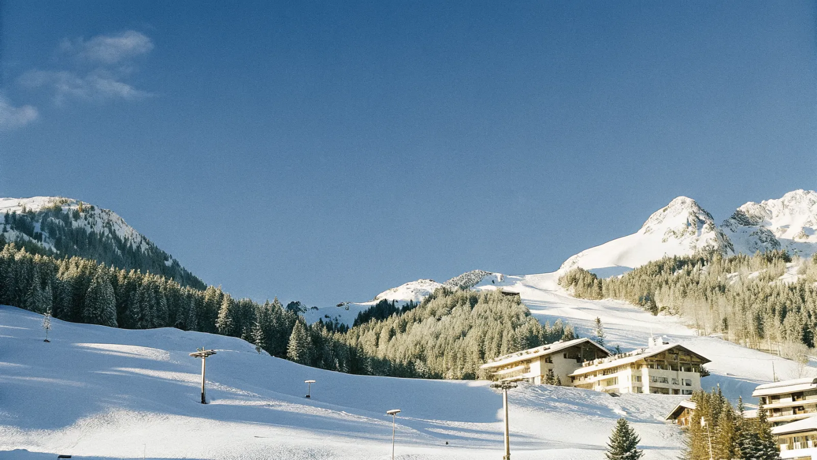 Sniega klātie Alpu kalni ar slēpošanas trasēm un zilām debesīm