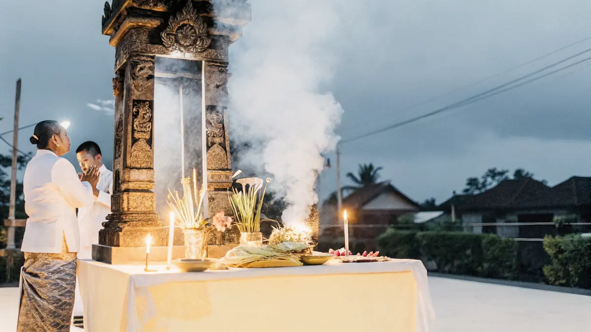 Canang sari ziedu upuru grozi pie akmens tempļa rītausmā ar vīraka dūmiem