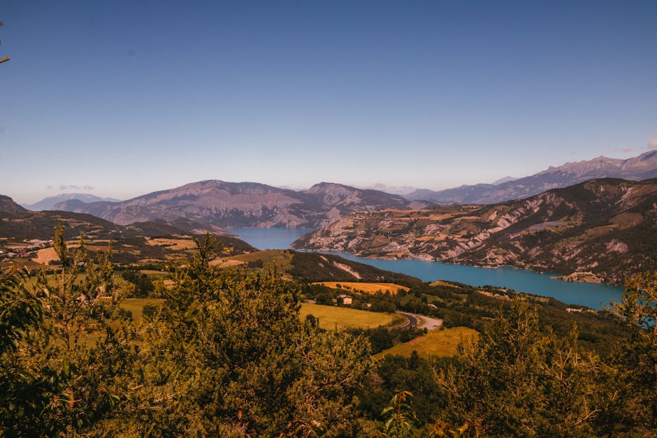 Ainavisks skats uz ezeru, ko ieskauj kalni un lauki, uzņemts no augstāka punkta.
